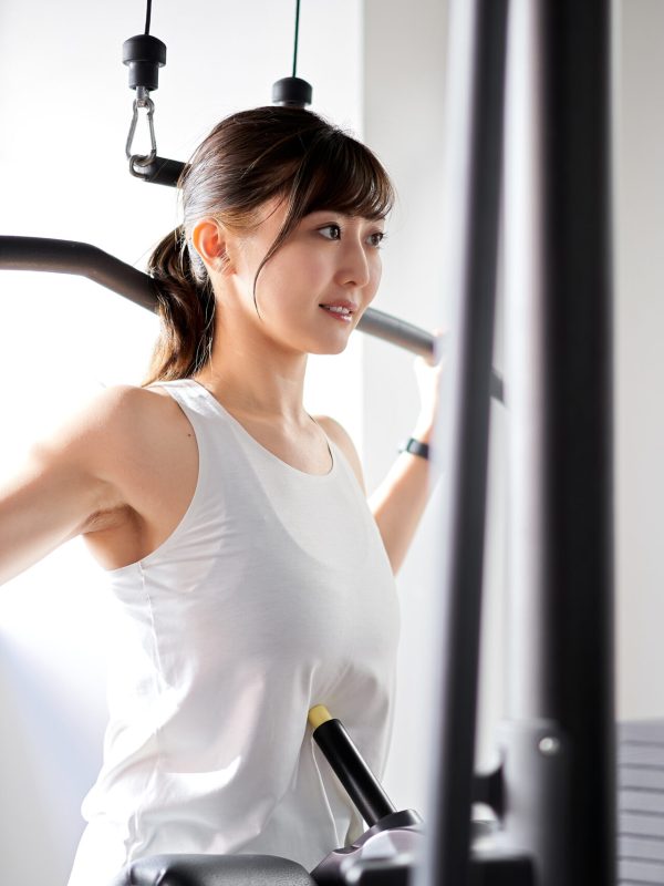 トレーニングジムでバックラットプルダウンをするアジア人女性
